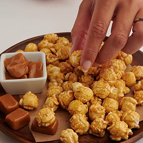 Hand picking caramel popcorn from a plate with caramel candies.