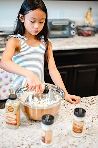 Young girl adding spices to a mixing bowl in the kitchen